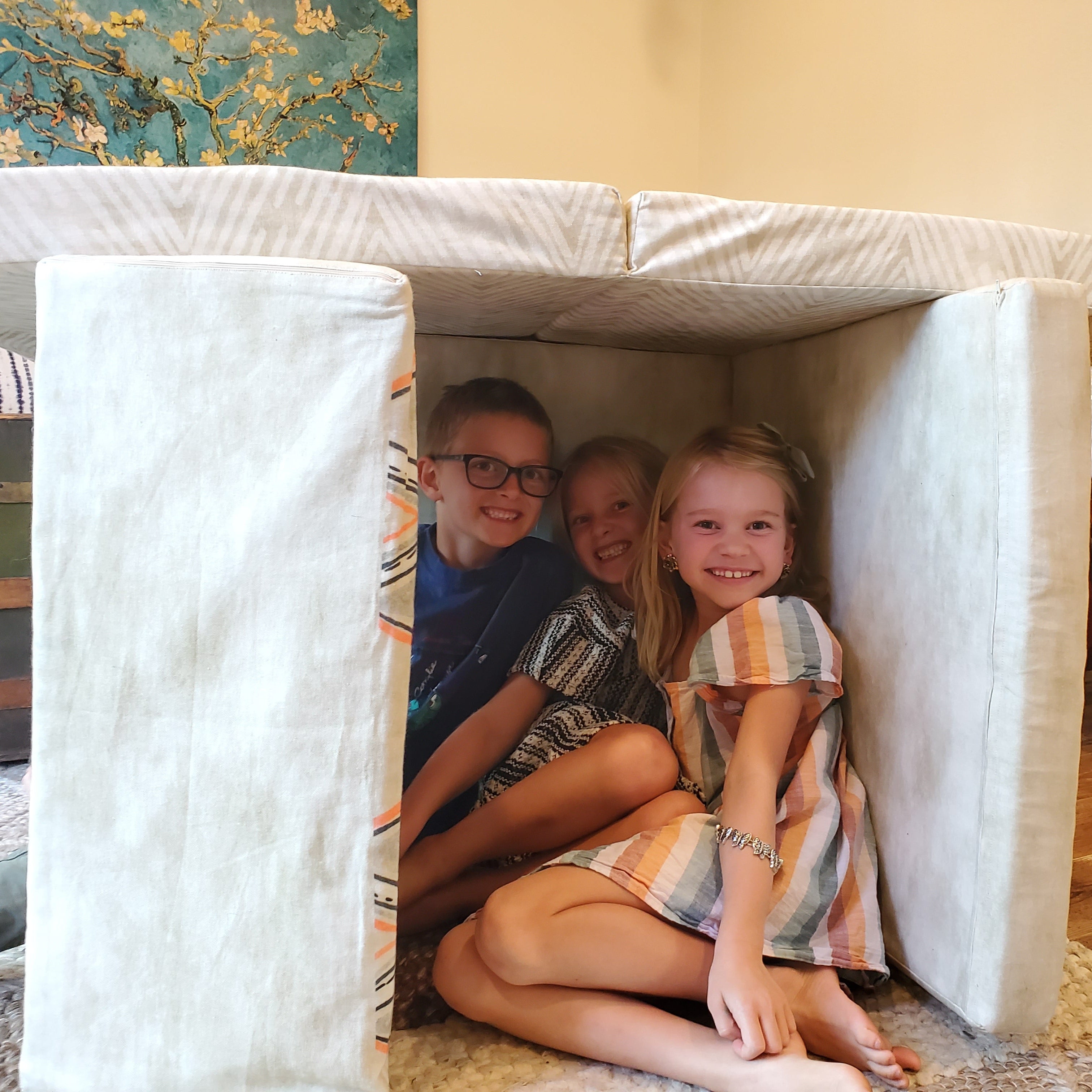 Children playing inside a play couch structure in a home setting.
