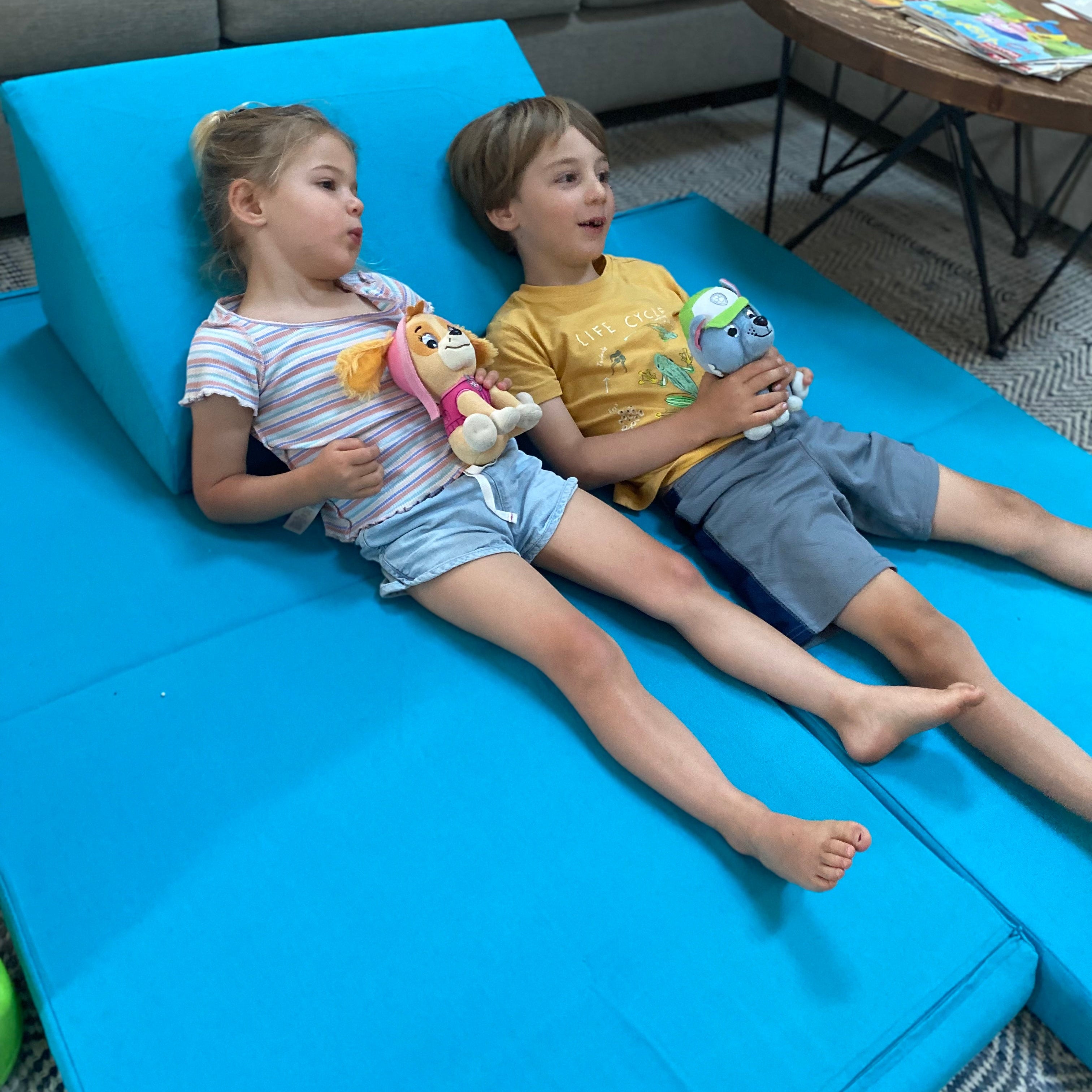 Two children lying on a blue Luna Lounger in a living room.